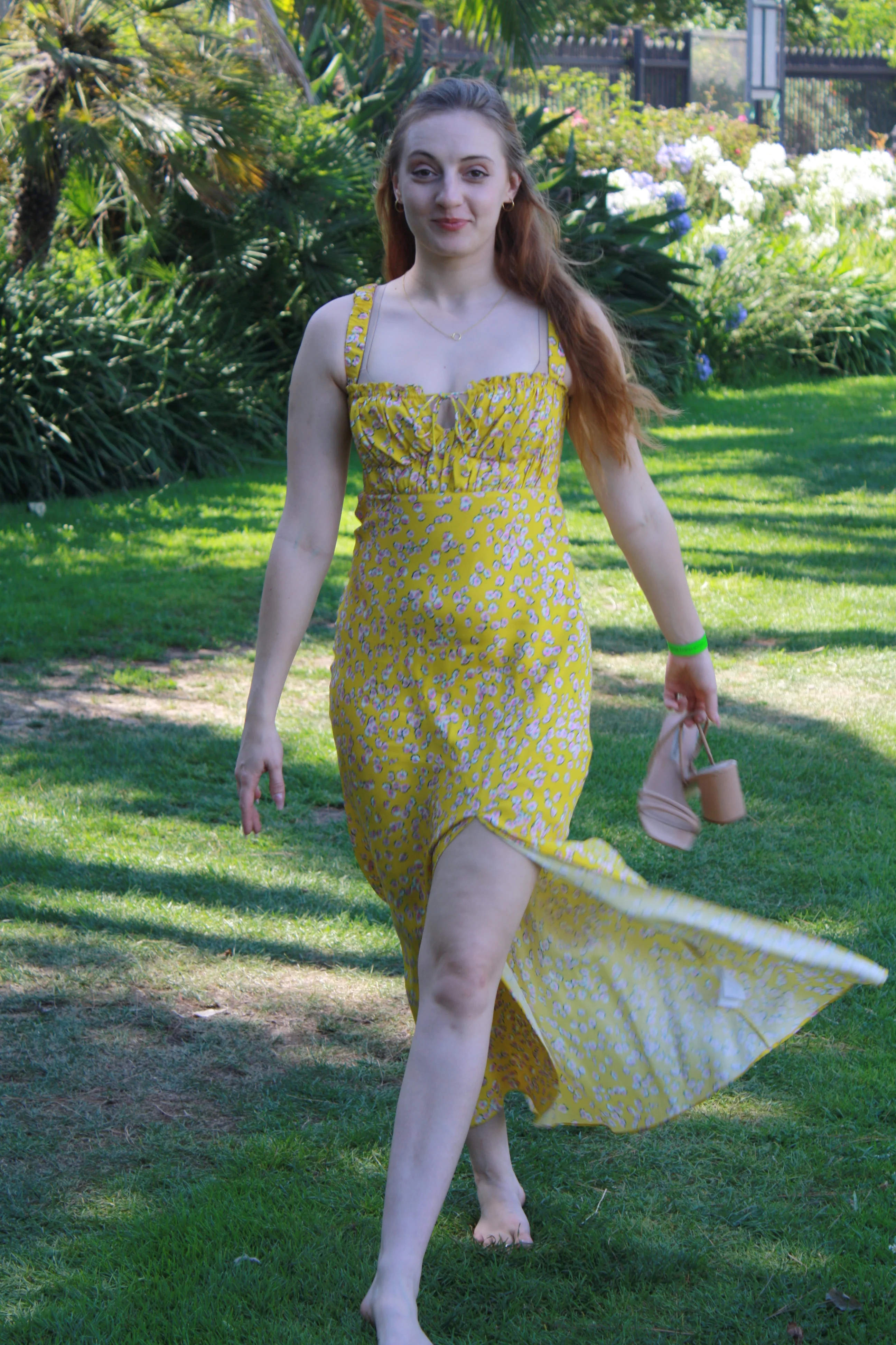 Jordie Morris walking barefoot with her yellow dress flowing to one side at the Exposition Park Rose Garden.
